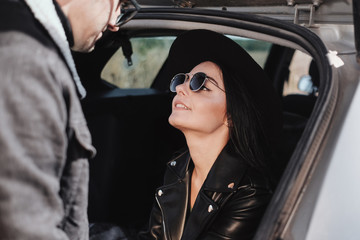 Fototapeta na wymiar Happy Traveling Couple Dressed in Black Stylish Clothes Enjoying a Car Trip on the Field Road, Vacation Concept