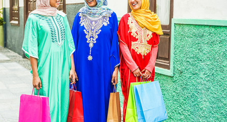 Fototapeta na wymiar Happy muslim friends going back at home after shopping - Young islamic girls having fun together - Sale, religion, culture and friendship concept - Focus on hands, bags