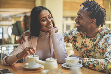 Happy black couple drinking coffee inside vintage bar restaurant - Trendy young people having fun talking and laughing at breakfast time - Love and lifestyle concept - Focus on woman face