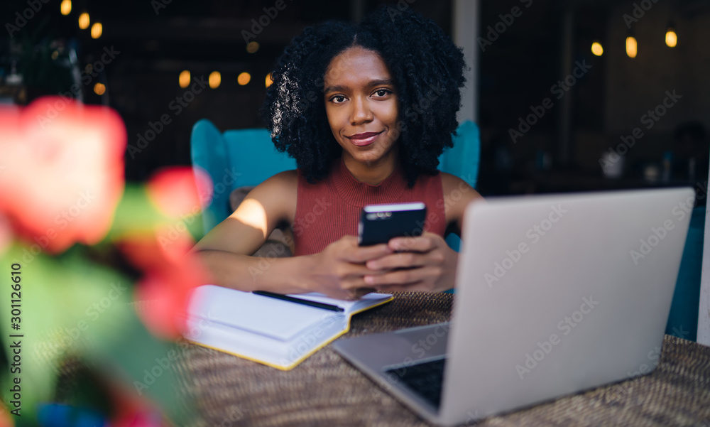 Aufkleber portrait of cheerful female blogger smiling at camera while sitting at table and spending time for c