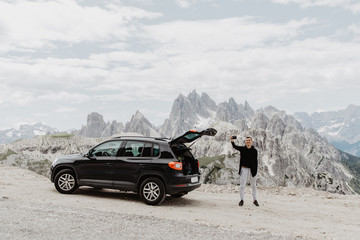 Young handsome man open trunk in his car to get stuff on the top of mountains road