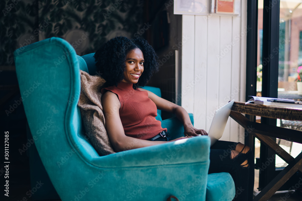 Poster portrait of cheerful female copywriter resting in big comfortable chair and smiling at camera during
