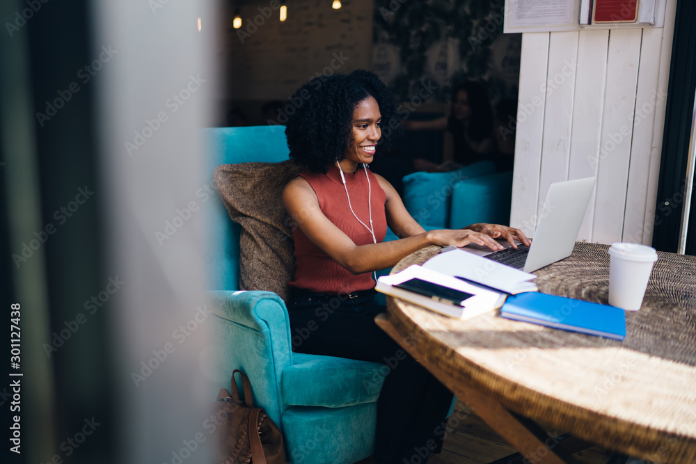 Poster side view of cheerful female blogger enjoying messaging with followers from website while listening 