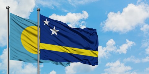 Palau and Curacao flag waving in the wind against white cloudy blue sky together. Diplomacy concept, international relations.