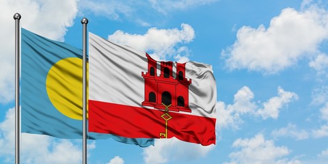 Palau and Gibraltar flag waving in the wind against white cloudy blue sky together. Diplomacy...