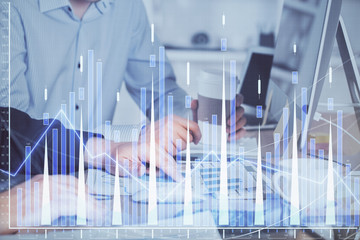 Multi exposure of chart with man typing on computer in office on background. Concept of hard work.