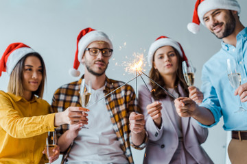 Fototapeta premium selective focus of cheerful businessmen and multicultural businesswomen holding sparklers and champagne glasses in office