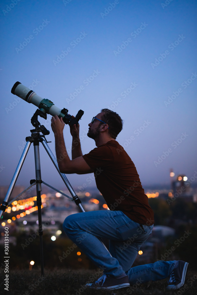 Canvas Prints astronomer with a telescope watching at the stars and moon with blurred city lights in the backgroun