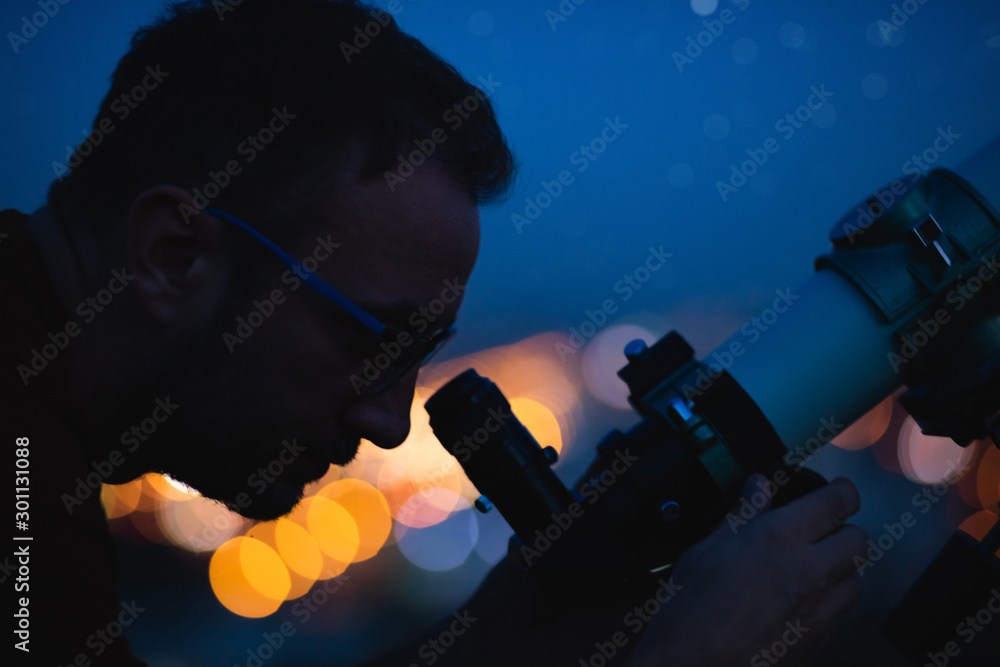 Wall mural astronomer with a telescope watching at the stars and moon with blurred city lights in the backgroun