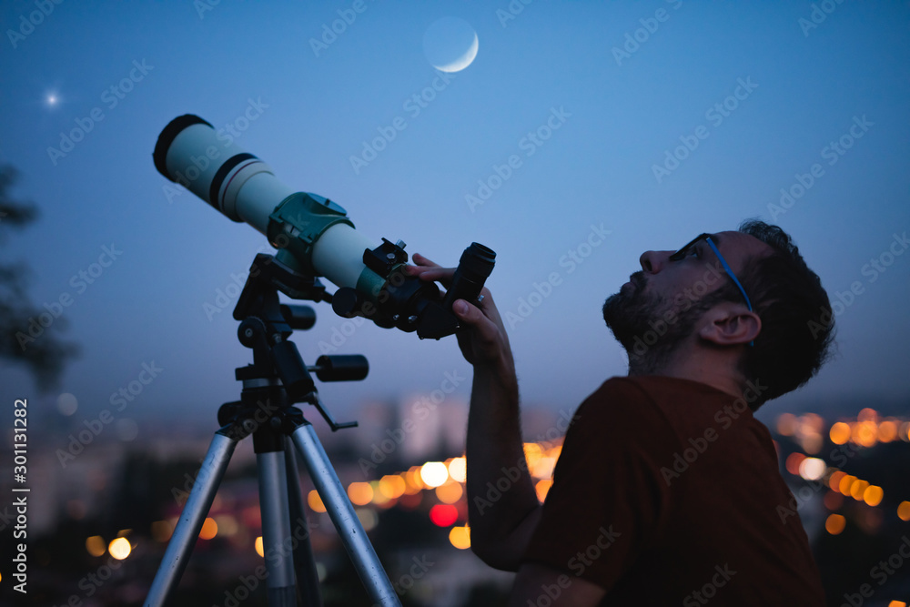 Canvas Prints astronomer with a telescope watching at the stars and moon with blurred city lights in the backgroun