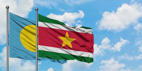 Palau and Suriname flag waving in the wind against white cloudy blue sky together. Diplomacy...
