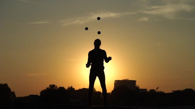 Circus artist juggling with balls on colorful sunset