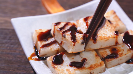 Pouring black soy sauce on ready-to-eat delicious turnip cake, Chinese traditional local dish radish cake in restaurant, close up, copy space.