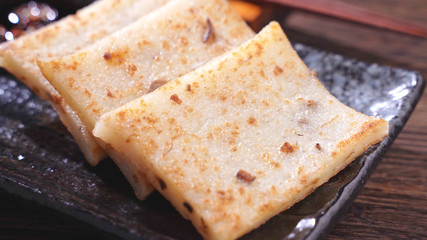 Pouring black soy sauce on ready-to-eat delicious turnip cake, Chinese traditional local dish radish cake in restaurant, close up, copy space.