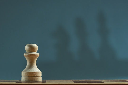 Chess pawn with blur shadow of king, Queen, horse on gray background. Photo with copy space.
