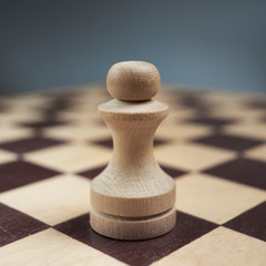 One white pawn close-up on a chessboard on a gray background. Background in blur.