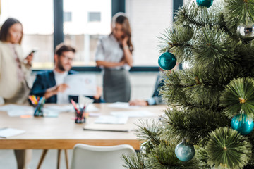 Selective focus of decorated Christmas tree near multicultural coworkers in office
