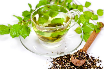 Glass cup of green tea with green natural birch branches and dry tea in a wooden spoon isolated on...