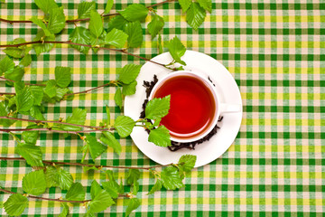 Black tea in a white cup with fresh natural birch branches on textile background. Top view.