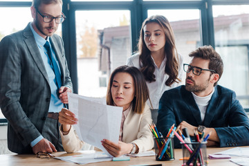 selective focus of businessmen looking at documents near multicultural businesswoman in office