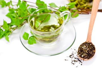 Glass cup of green tea with green natural birch branches and dry tea in a wooden spoon isolated on a white background. 