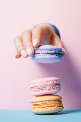 Beautiful girl hands with trendy manicure nail holding color macaroon cake through hole in pink...