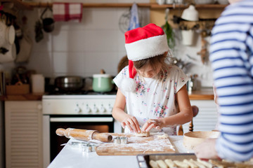 Child chef is cooking Christmas cookies in cozy home kitchen. Kid in santa hat is enjoying preparation holiday meal for family. Little girl is baking Xmas pastry from dough. Lifestyle moments.