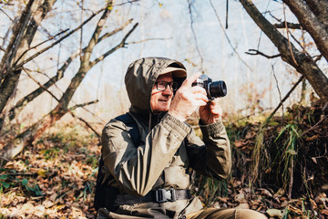 Fototapeta premium Senior man taking photo in nature. Mature man taking pictures of the forest in fall.