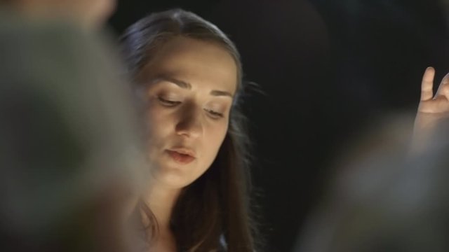 Handheld shot of female art teacher drawing sand art on lightbox and talking to unrecognizable children in dark classroom