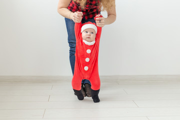 Children, childhood and holidays concept - baby in christmas clothes making first steps