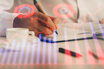 Double exposure of man's hands writing notes of stock market with forex chart.