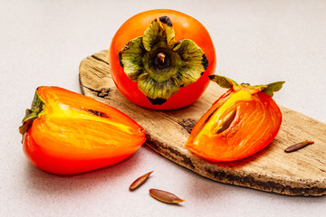 Ripe single persimmon. Fresh whole fruit, half sliced, seeds. Wooden cutting board, stone concrete...