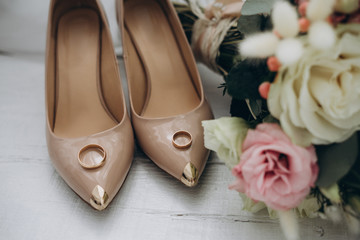 bridal shoes with wedding rings near the bride’s bouquet