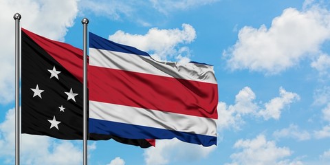 Papua New Guinea and Costa Rica flag waving in the wind against white cloudy blue sky together. Diplomacy concept, international relations.