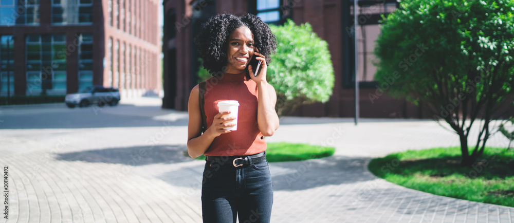 Poster half length portrait of cheerful female student with takeaway cup in hand smiling at camera while ma
