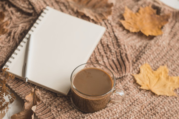Autumn background with space for text. Notepad with blank sheets for notes with coffee, sweater and autumn leaves.
