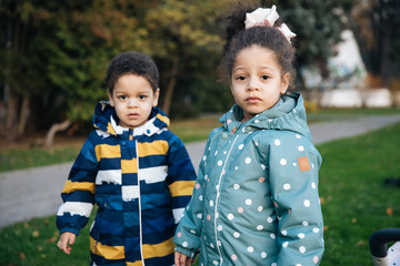 Little beautiful children on a walk, kids walk with baby carriages on the green grass, emotional portrait