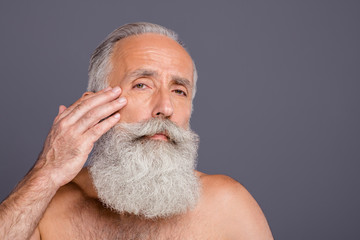 Close up portrait of concentrated focused serious old man caring about his facial skin smooting...