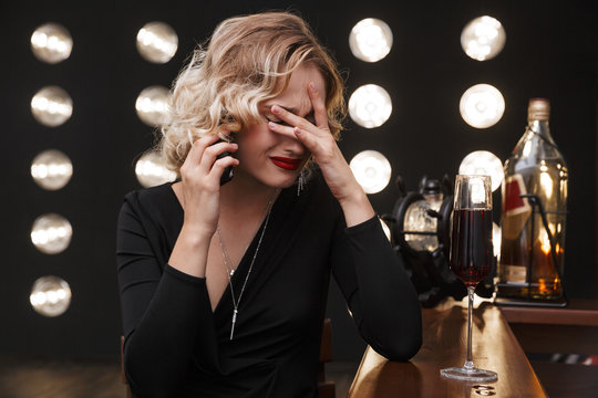 Image of confused blonde woman crying and talking on cellphone in bar