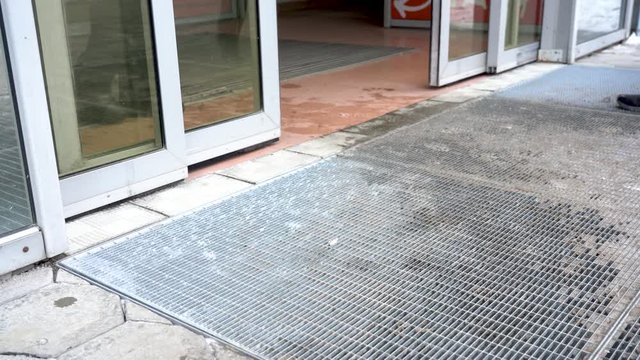 Automatic glass doors open and close. Entrance to the mall. Winter. Wet footprints on the floor. The legs of many passers-by