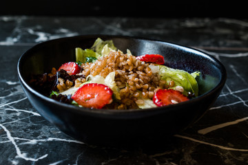 Buckwheat Salad with Strawberry Slices and Green Leaves in Black Bowl on Dark Granite Surface.