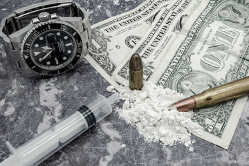 Mock-up concept of illegal drug dealing on a work surface. An expensive, swiss-made watch can be seen next to dollar bills used in the illegal drugs trade.