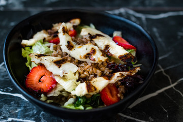 Grilled Halloumi Cheese Salad with Strawberry Slices and Buckwheat / Hellim in Black Bowl on Dark Granite Surface.