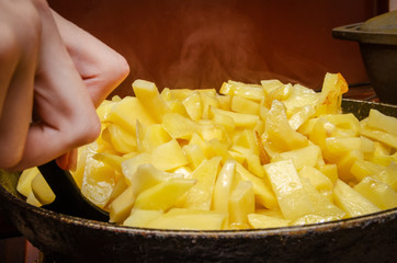 woman's hand with a black spatula stirs potatoes while frying in a frying pan close up