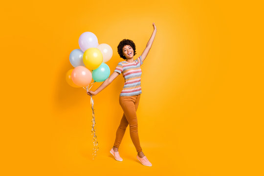 Full length photo of positive cheerful girl hold many baloons have summer free time walk with her boyfriends feel content wear striped t-shirt outfit isolated over yellow color background