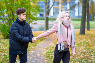 Two teenagers in love in quarrel. The blonde girl takes offense at boy, guy holds her hand, asks...