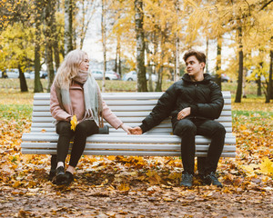 Young beautiful bevushka blonde and young handsome brunette guy make up after a quarrel. Sitting on park bench. The concept of teenage love and reconciliation