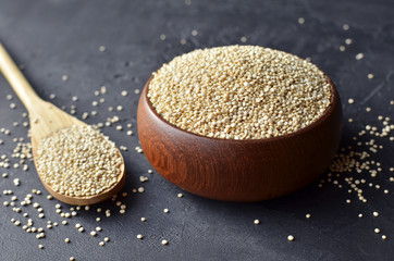 Uncooked organic quinoa grains in wooden bowl and spoon on dark stone background. Cooking ingredients, healthy food.