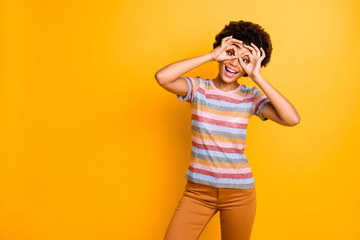 Portrait of positive cheerful afro american girl make ok sign look through binoculars look like spy feel childish wear casual style clothes isolated over bright color background