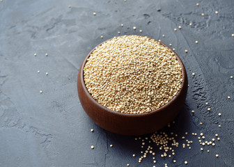 Quinoa in a brown wooden bowl on dark stone background. Dry uncooked cereal grains, cooking...